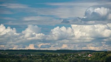 Kırsal alandaki küçük evlerin üzerinde mavi gökyüzünde hızla ilerleyen beyaz kabarık kümülüs bulutlarının hızlandırılmış görüntüleri.