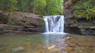 Yazın yağmur ormanlarında kayalık kayalıklardan dökülen beyaz köpüklü suyla dağ nehrindeki muhteşem şelale manzarası..