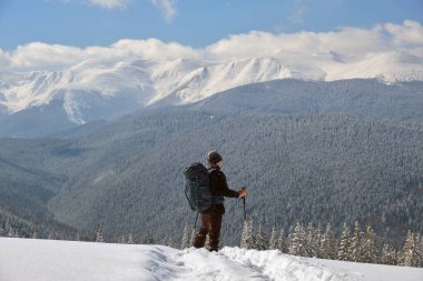 Sırt çantalı bir adam soğuk kış gününde dağ yamacında yürüyüş yapıyor..