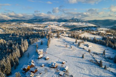 Geceleri soğuk dağlarda karla kaplı ormanlar arasında küçük köy evleri olan havadan kış manzarası..