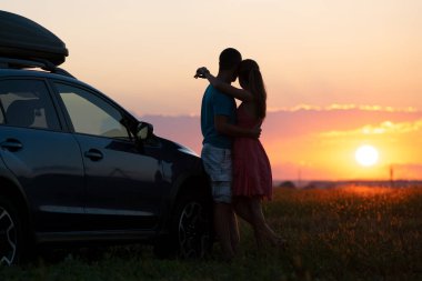 Gün batımında arabalarının yanında duran mutlu çift. Genç bir adam ve bir kadın birlikte vakit geçiriyorlar..