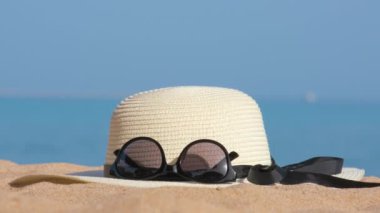 Sıcak, güneşli bir günde, tropik deniz kıyısındaki kumlu kumsalda sarı hasır şapka ve siyah koruyucu güneş gözlüğü. Yaz tatili kavramı