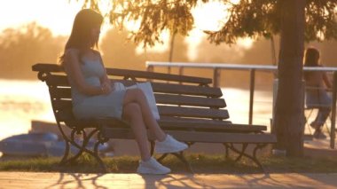 Sıcak bir akşamda gölün kenarında tek başına oturan, yaz elbisesi içindeki üzgün genç kadın. Yalnızlık ve dinlenme günlük acele kavramından