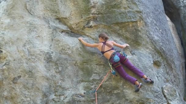 Beslutsam flicka klättrare klamrar upp brant vägg av steniga berg. Sportkvinnan övervinner svår väg. Engagera sig i extrema sporter och bergsklättring hobby koncept — Stockvideo