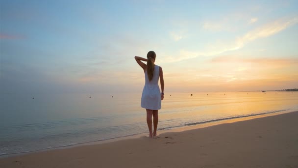 Самотня молода жінка стоїть на піщаному пляжі біля моря насолоджуючись теплим тропічним вечором — стокове відео