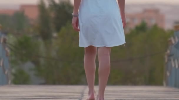 Primer plano de la mujer joven en vestido blanco que va a dar un paseo en el muelle largo en la orilla del mar por la noche. Concepto de vacaciones y viajes — Vídeos de Stock