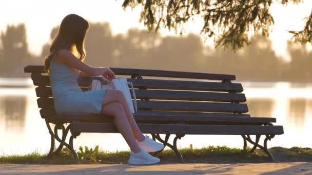 Samotna kobieta siedząca na ławce nad jeziorem ciesząca się ciepłym letnim wieczorem. Pojęcie samotności i relaksu — Wideo stockowe