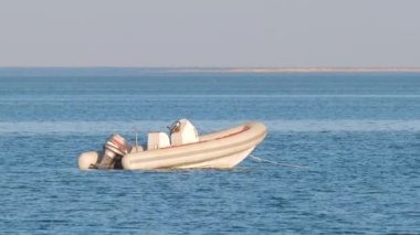 Mavi deniz suyunun dalgalı yüzeyi ve durgun dalgalarda yüzen beyaz sürat teknesiyle deniz manzarası..