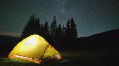 Gece yıldızlarının altındaki karanlık dağlardaki kamp alanında parlayan parlak kamp çadırının zaman atlaması. Aktif yaşam tarzı ve yürüyüş konsepti.