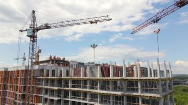 İnşaat halindeki yüksek beton binadaki vinçler ve profesyonel işçiler. Gayrimenkul geliştirme kavramı.
