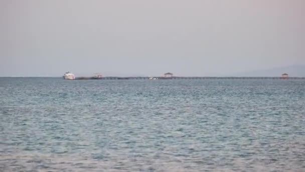 Seascape com superfície ondulada de água do mar azul com navio distante no final do longo cais flutuando em ondas calmas — Vídeo de Stock