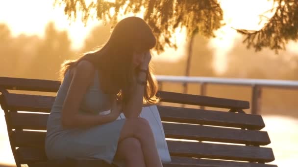 Одинокая несчастная молодая женщина, сидящая одна на скамейке в парке теплым летним вечером. Одиночество и отдых в природе. — стоковое видео