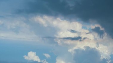 Beyaz kabarık kümülüs bulutlarının parlak manzarası mavi gökyüzünde güçlü rüzgarın altında şekilleniyor ve değişiyor.