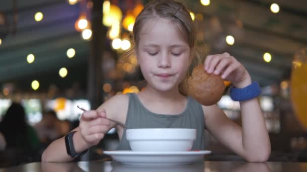 Kind meisje eet soep en lekkere hamburger in restaurant — Stockvideo