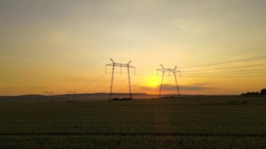 Gün batımında elektrik hatları olan yüksek voltaj kuleleri.