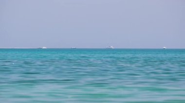 Mavi deniz suyunun dalgalı yüzeyi ve sakin dalgalar üzerinde yüzen uzak gemileri olan deniz burnu.