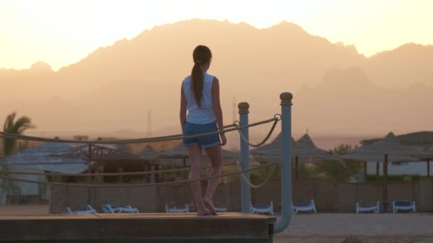 Ung kvinnlig turist i avslappnade kläder njuter av varm solig kväll på stranden. Sommarsemester och resekoncept — Stockvideo