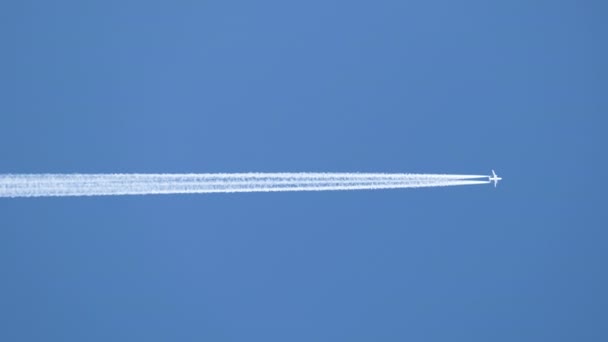 Aereo a reazione passeggeri distanti che volano in alta quota su cielo blu chiaro lasciando tracce di fumo bianco di contrail dietro. Concetto trasporto aereo — Video Stock