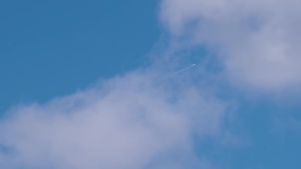 Μακρινό επιβατικό αεροπλάνο που πετά σε μεγάλο υψόμετρο στον γαλάζιο ουρανό με λευκά σύννεφα αφήνοντας ίχνη καπνού πίσω του. Έννοια αεροπορικών ταξιδιών — Αρχείο Βίντεο