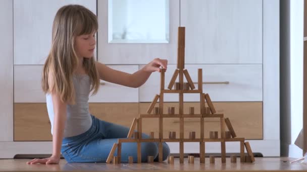 Ευτυχισμένο κορίτσι παιδί παίζει παιχνίδι στοίβαγμα ξύλινα μπλοκ παιχνιδιών σε υψηλή δομή σωρό. Χειροκίνητος έλεγχος κίνησης και δημιουργία υπολογιστικών δεξιοτήτων — Αρχείο Βίντεο