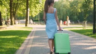 Yaz günü yeşil bavulla parkta yürüyen genç bir kadın. Seyahat ve tatil kavramı.