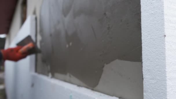 İnşaat işçisi ev duvarını yapışkan çimento yapıştırıcısıyla kaplıyor berore termal koruma için köpük yalıtım çarşafları yerleştiriyor. — Stok video