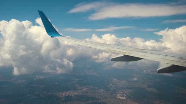 Pohled na křídlo tryskového letadla zevnitř letící přes bílé opuchlé mraky na modré obloze. Koncept cestování a letecké dopravy — Stock video