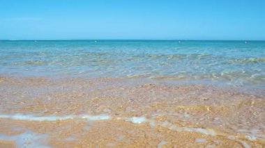 Mavi deniz suyunun yüzeyi ve küçük dalgalı dalgaların sarı kumsala çarptığı deniz burnu. Seyahat ve tatil kavramı