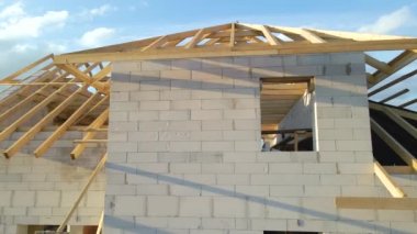 Havalandırılmış hafif beton duvarları ve yapım aşamasındaki ahşap çatı iskeleti olan bitmemiş özel evin havadan görüntüsü.