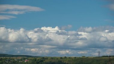 Kırsal alandaki küçük evlerin üzerinde mavi gökyüzünde hızla ilerleyen beyaz kabarık kümülüs bulutlarının hızlandırılmış görüntüleri