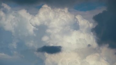 Beyaz kabarık kümülüs bulutlarının parlak manzarası mavi gökyüzünde güçlü rüzgarın altında şekilleniyor ve değişiyor.