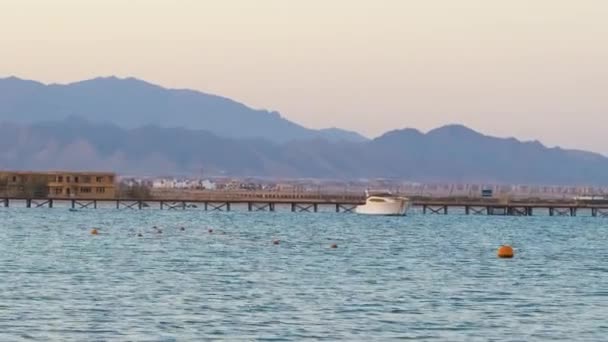 Seascape s vlnitým povrchem modré mořské vody se vzdálenou lodí na konci dlouhého mola plovoucího na klidných vlnách — Stock video