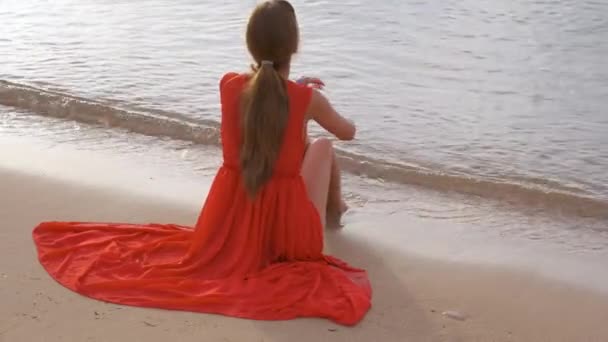 Samotna młoda kobieta siedzi na piaszczystej plaży nad morzem ciesząc się ciepłym tropikalnym wieczorem — Wideo stockowe