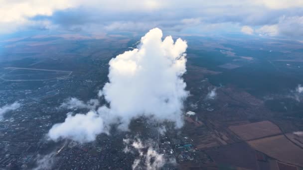 Luchtfoto vanuit vliegtuigraam op grote hoogte van verre stad bedekt met gezwollen cumulus wolken vormen zich voor regenbui — Stockvideo