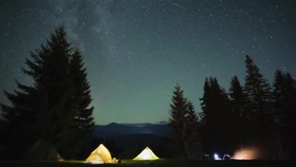 夜の空の下、暗い山の中で輝く星とキャンプ場の照明付きの観光テントの近くでたき火を燃やす以外にも、ハイカーの膝の崩壊。アクティブなライフスタイルと屋外生活のコンセプト — ストック動画