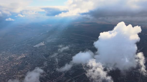 Вид с воздуха из окна самолета на большой высоте далекого города, покрытый белыми кучевыми облаками — стоковое видео