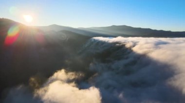 Sisli ve hızlı bulutların üzerindeki hava manzarası gün batımında dağ tepelerini kaplıyor.