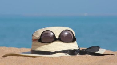 Sıcak, güneşli bir günde, tropik deniz kıyısındaki kumlu kumsalda sarı hasır şapka ve siyah koruyucu güneş gözlüğü. Yaz tatili kavramı