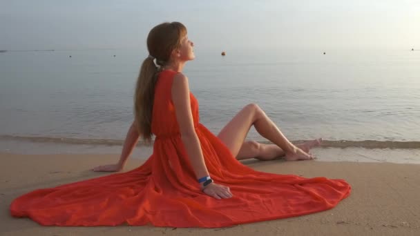 Jeune femme seule assise sur la plage de sable de l'océan au bord de la mer profitant d'une chaude soirée tropicale — Video