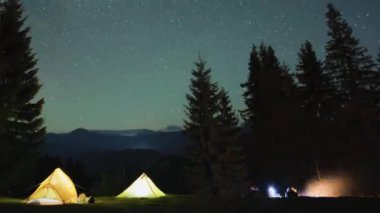 Yürüyüşçülerin dinlenme zamanı. Aydınlanmış turist çadırlarının yanındaki parlak şenlik ateşinin yanı sıra parlayan yıldızlarla dolu gece gökyüzünün altındaki dağ ormanlarında kamp yapıyorlar. Aktif yaşam tarzı ve açık hava yaşam konsepti