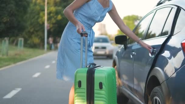 Ung kvinna förare sätta grön resväska inne i bilen på stadens gata. Resor och semestrar koncept — Stockvideo