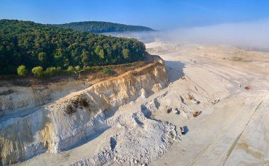 Kazı araçları ve çöp kamyonları ile inşaat endüstrisi için kireçtaşı malzemelerinin açık çukur madenciliğinin hava görüntüsü.