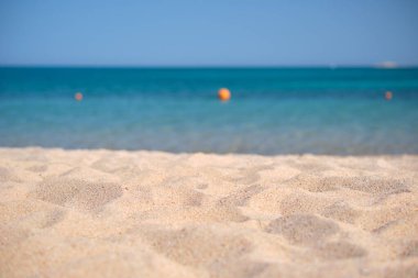 Arka planda mavi deniz suyuyla sahil sahilini kaplayan temiz sarı kum yüzeyini kapatın. Seyahat ve tatil kavramı.