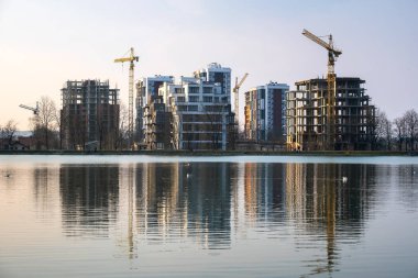 Göl kıyısında inşaat halindeki vinçler ve yüksek konutlu binalar. Gayrimenkul geliştirme.