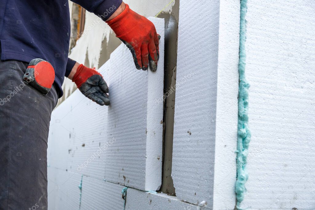 Construction worker installing styrofoam insulation sheets on house facade wall for thermal protection.