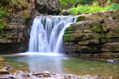 Yaz ormanlarında kayalık oluşumdan dökülen köpüklü suyla birlikte dağ nehrine dökülen şelale..