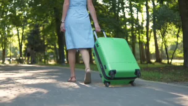 Nahaufnahme einer jungen Frau, die an einem Sommertag mit grünem Koffer auf dem Bürgersteig der Stadt läuft. — Stockvideo