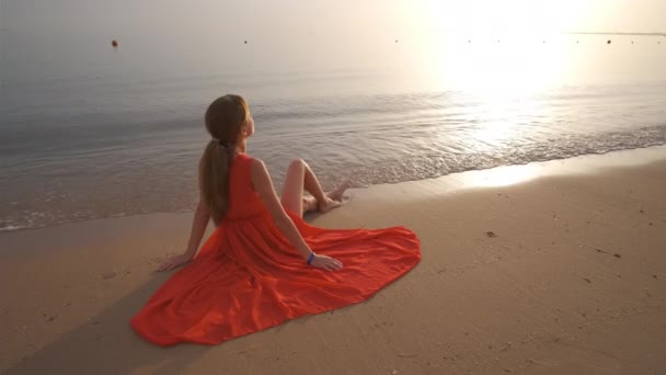 Young happy woman wearing red dress resting on sea beach enjoying warm summer morning. — Stock Video