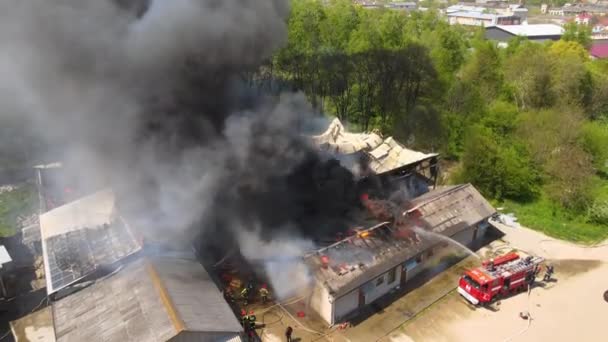 Повітряний вигляд пожежників, що гасять зруйновану будівлю під вогнем зруйнованого даху і піднімається темний дим — стокове відео