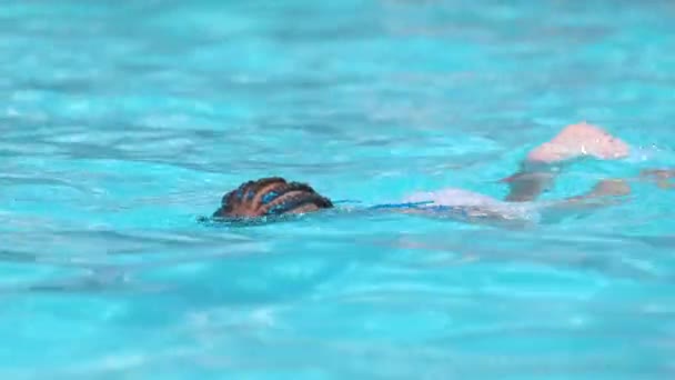 Маленькая девочка пытается плавать в бассейне с чистой голубой водой. Концепция летних мероприятий — стоковое видео